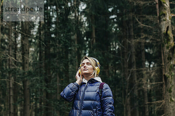 Junge Frau genießt Musik über Kopfhörer im Wald