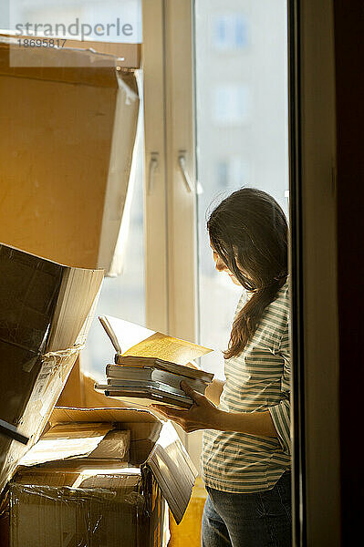Frau packt Bücher in Kartons  gesehen durchs Fenster