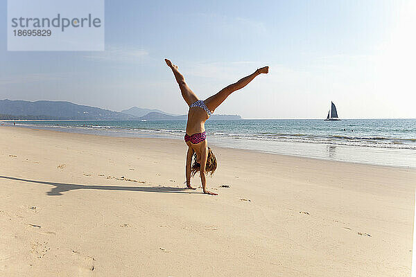 Junge Frau im Bikini übt Handstand am Strand