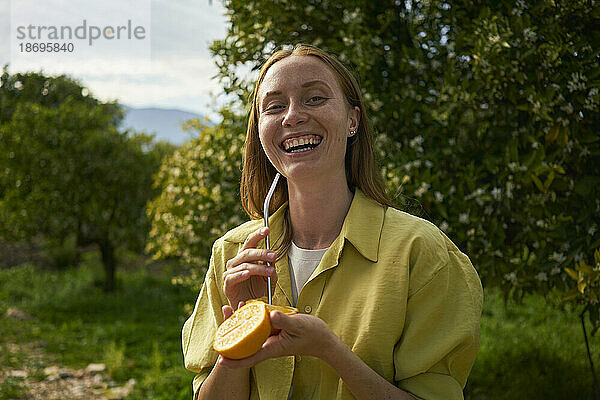 Glückliche Frau mit wiederverwendbarem Metallstroh und Orangenscheiben im Obstgarten