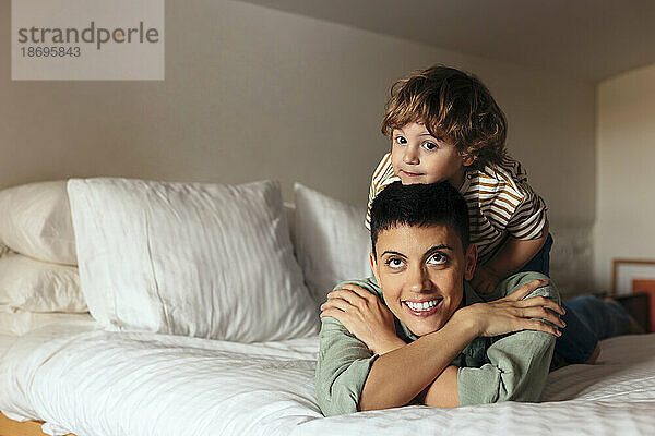 Smiling woman lying with son on bed at home
