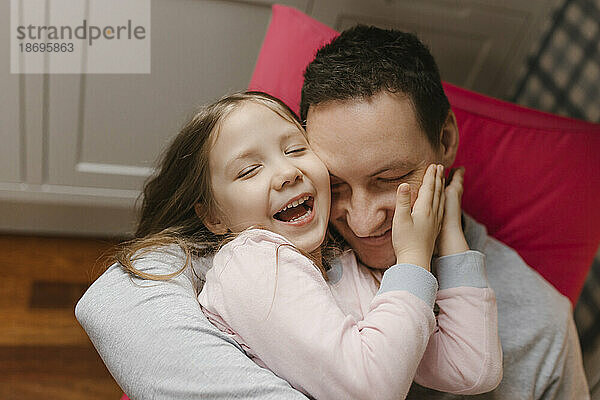 Playful father and daughter embracing with eyes closed at home