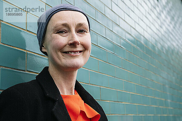 Lächelnder Krebspatient mit Kopftuch an einer Ziegelwand