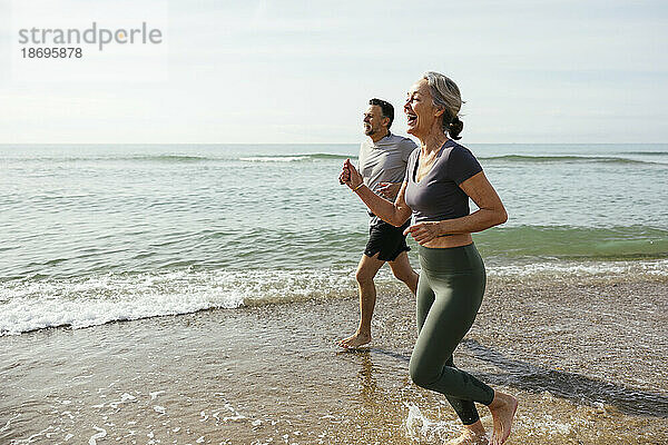 Glückliches älteres Paar  das am Strand lacht und im Wasser läuft