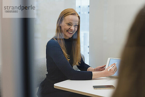 Glückliche Geschäftsfrau zeigt Tablet-PC im Büro sitzend