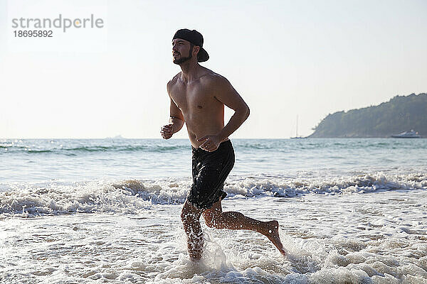 Hemdloser Mann läuft am Strand im Wasser