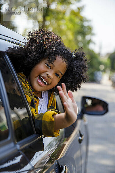 Glückliches Mädchen mit lockigem Haar lehnt vor dem Autofenster