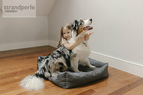 Mädchen umarmt australischen Schäferhund zu Hause auf dem Haustierbett