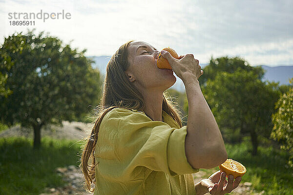 Frau isst frische saftige Orange im Obstgarten