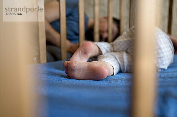 Boy sleeping in crib with father in background at home