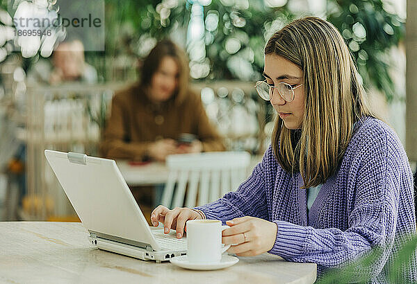 Mädchen hält Kaffeetasse mit Laptop in der Schulkantine