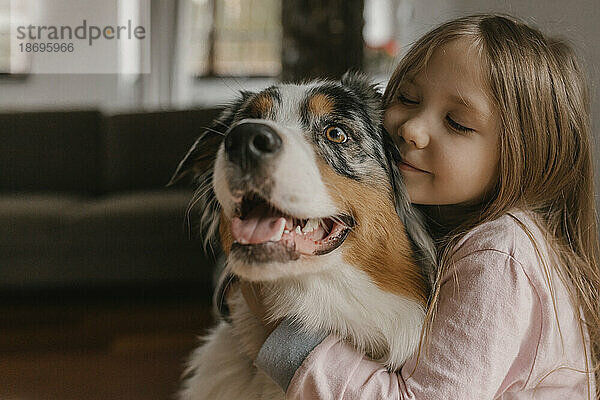 Mädchen umarmt australischen Schäferhund zu Hause