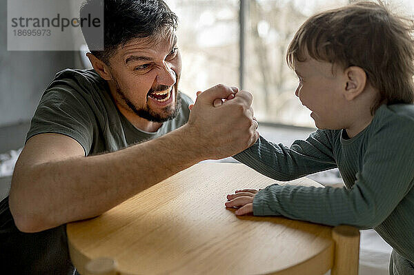 Aufgeregter Vater beim Armdrücken mit Sohn zu Hause