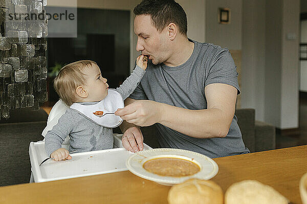 Vater füttert kleinen Jungen am Esstisch mit Suppe