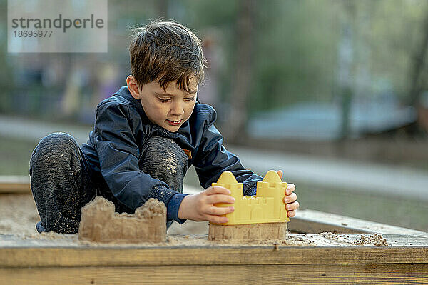 Junge baut Sandburg mit Spielzeug im Park