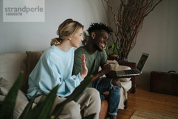 Glückliches Paar gestikuliert bei Videoanruf über Laptop zu Hause