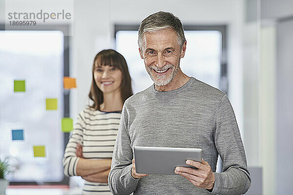 Lächelnder älterer Geschäftsmann hält Tablet-PC mit Kollegen am Arbeitsplatz
