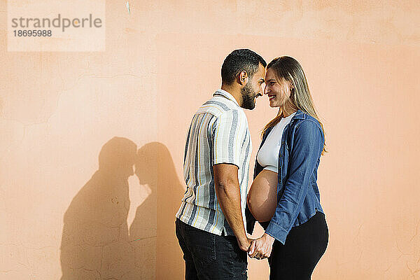 Happy pregnant woman standing with man in front of wall