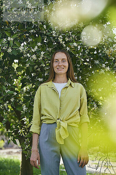 Young smiling woman standing in front of tree at garden
