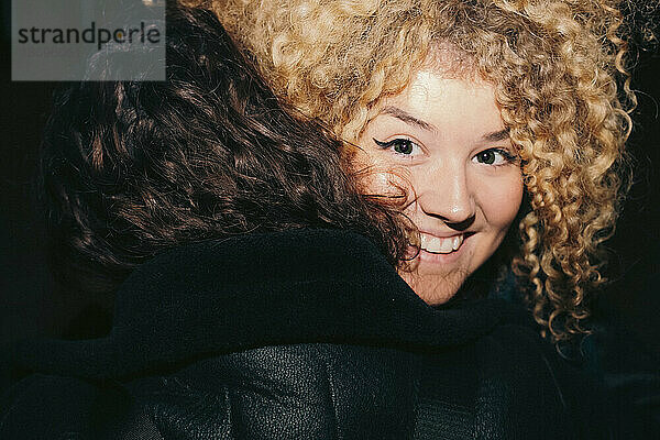 Lächelnde junge Frau mit lockigem Haar  die einen Freund umarmt