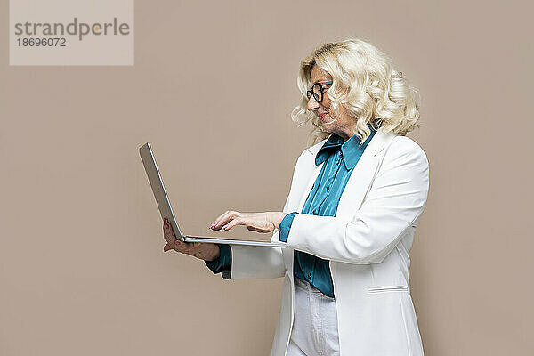 Ältere Geschäftsfrau benutzt Laptop vor farbigem Hintergrund