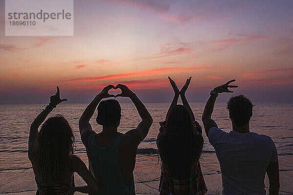 Freunde machen Liebestextschild mit Händen am Strand bei Sonnenuntergang