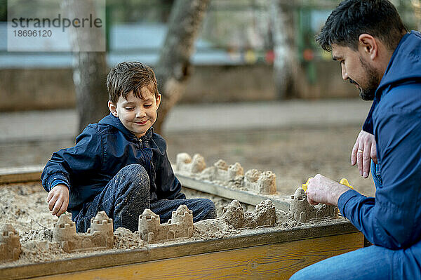 Vater und Sohn bauen Sandburgen im Sandkasten im Park