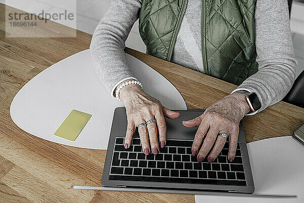 Hände einer älteren Frau  die zu Hause über den Laptop online einkauft
