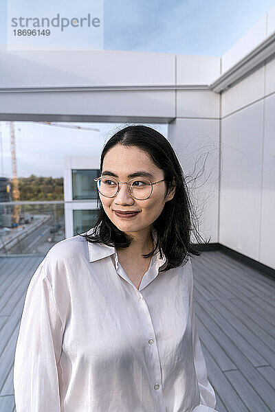 Nachdenkliche junge Geschäftsfrau im weißen Hemd auf der Terrasse eines Bürogebäudes