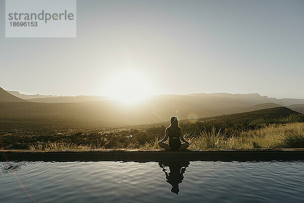 Frau macht Yoga und sitzt bei Sonnenuntergang am Pool