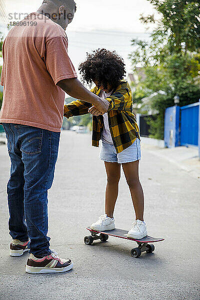 Vater hilft Tochter beim Stehen auf dem Skateboard am Fußweg