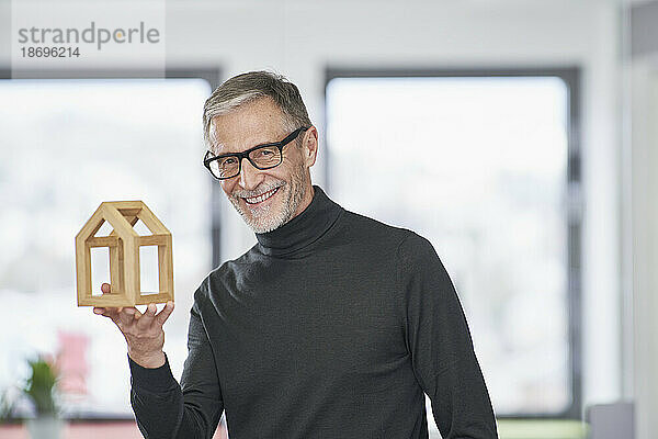 Porträt eines lächelnden leitenden Architekten  der ein Musterhaus im Büro hält