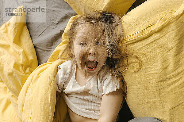 Blond girl screaming on bed by pillow at home