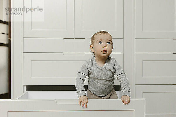 Kleiner Junge steht zu Hause in der Schublade des Kleiderschranks