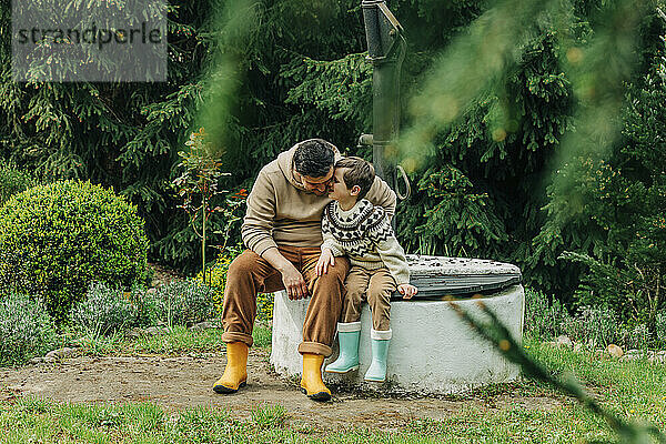 Son whispering to father sitting on well in garden