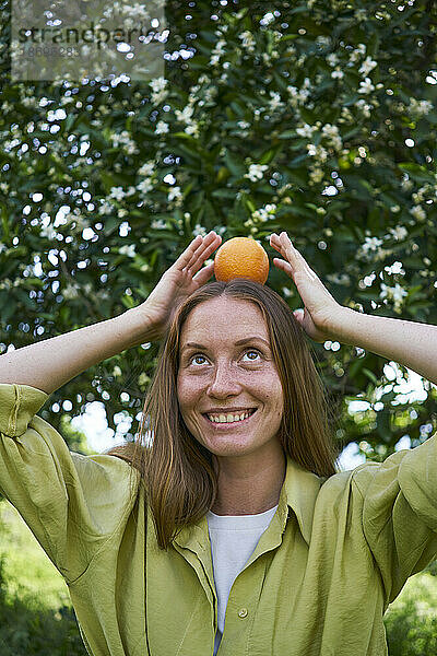 Frau balanciert Orange auf dem Kopf im Garten