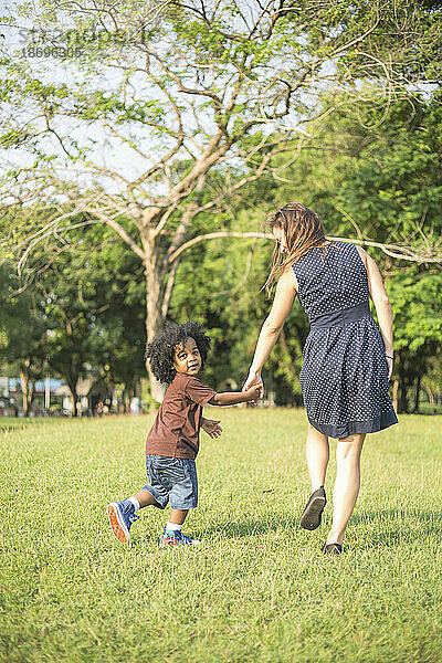 Mutter und Sohn halten sich an den Händen und gehen auf dem Gras im Park