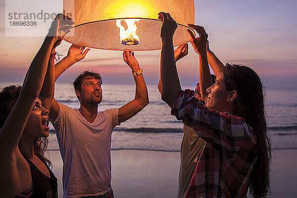 Freunde halten brennende Papierlaterne am Strand
