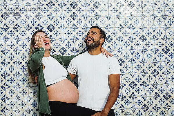 Pregnant woman having fun with man in front of patterned tiled wall