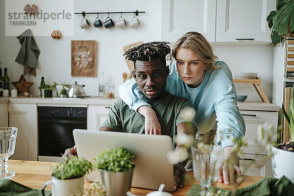 Junger Mann teilt Laptop mit Freundin in der heimischen Küche