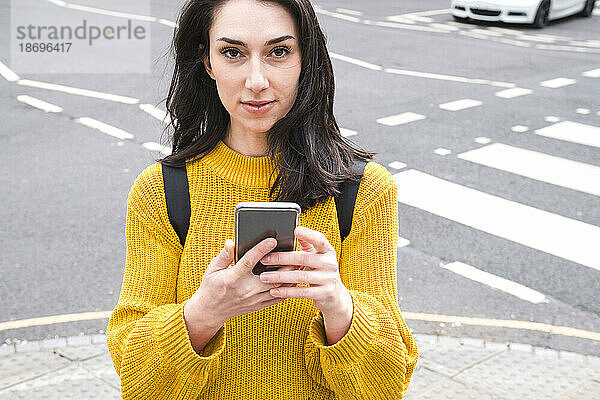 Junge Frau im gelben Pullover hält Smartphone in der Nähe der Straße