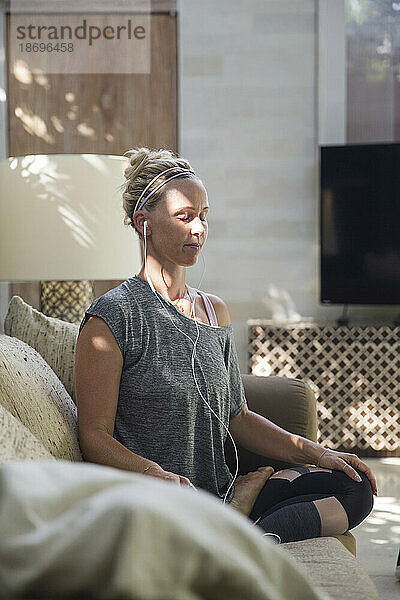Frau meditiert zu Hause auf dem Sofa