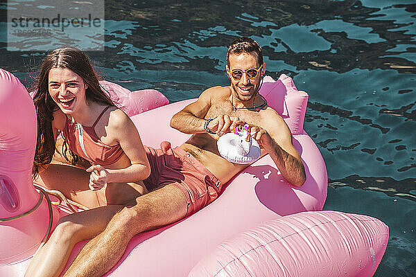 Paar schwimmt an sonnigem Tag auf Flamingo-Luftmatratze im Meer