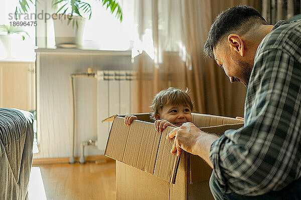 Father playing with son sitting in cardboard box at home