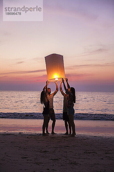 Freunde brennen Papierlaterne und stehen bei Sonnenuntergang am Strand