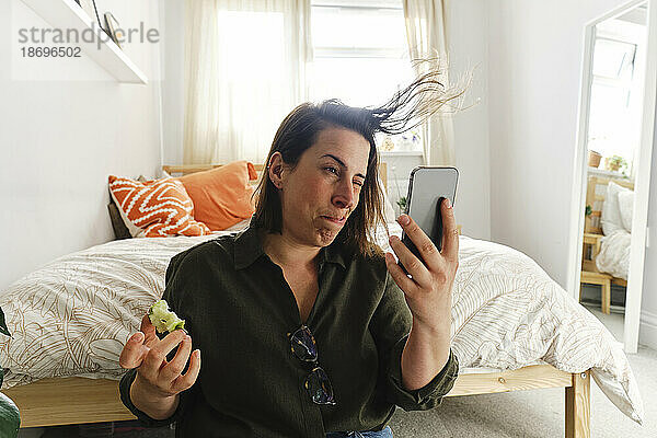 Frau bläst Haare und macht zu Hause ein Selfie mit dem Smartphone