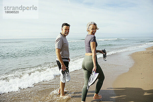 Älteres Paar mit Sportschuhen  das an einem sonnigen Tag in Küstennähe spaziert