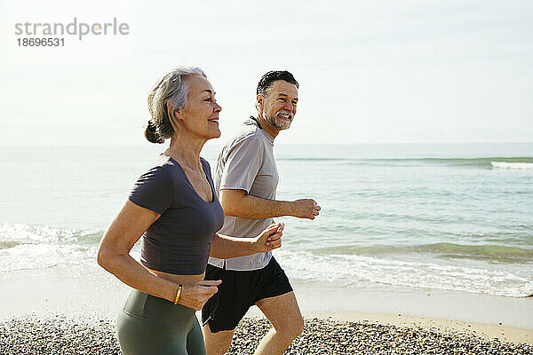 Lächelndes älteres Paar läuft am Strand