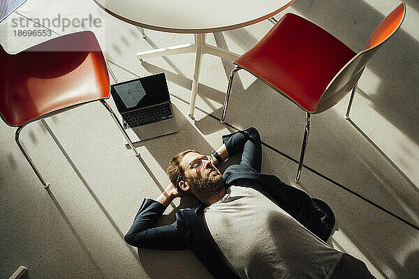 Geschäftsmann entspannt sich auf dem Boden mit Laptop und Stühlen im Büro