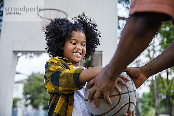 Lächelndes Mädchen nimmt Basketball vom Vater auf dem Sportplatz